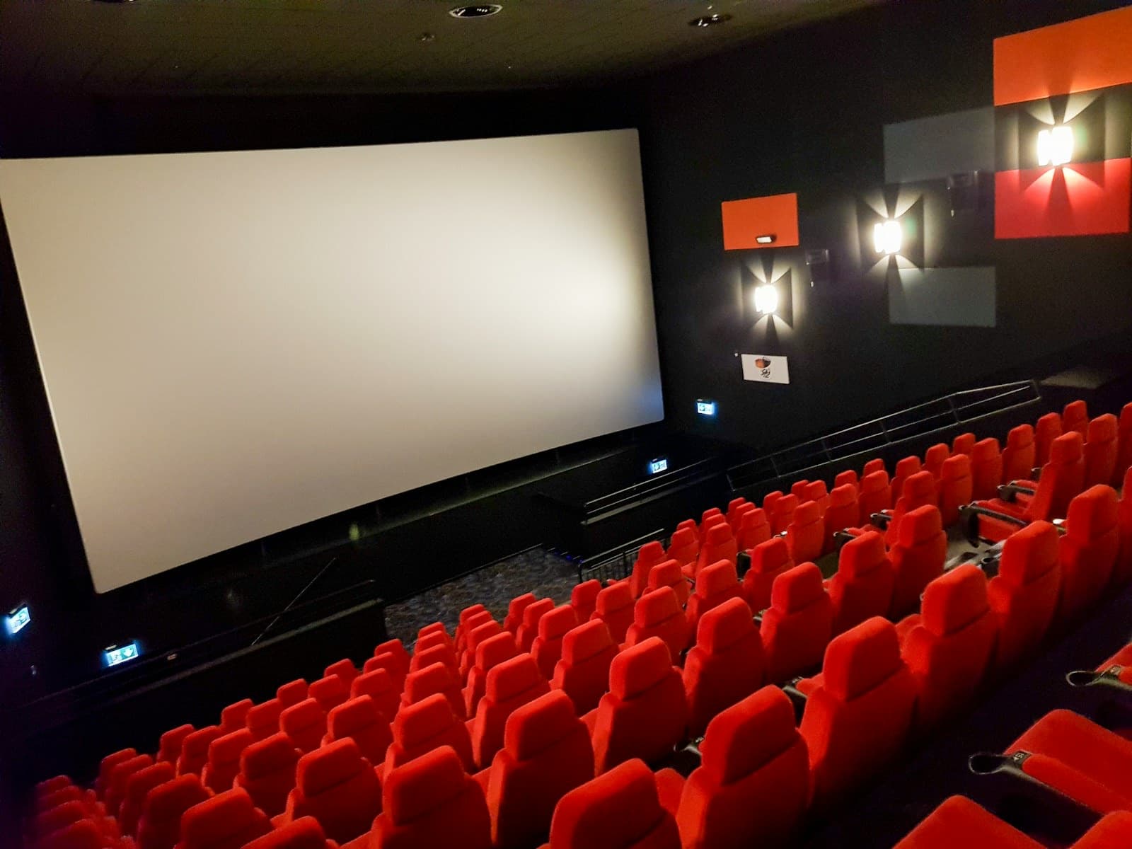 An empty cinema with rows of red seats facing the screen
